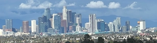 A skyline image of downtown LA with sunny skies and small clouds.