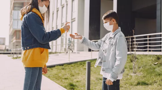 Two youth are shown with masks, using hand sanitizer
