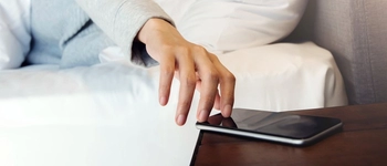 Image of a person's hand, reaching for a phone on a bedside table.