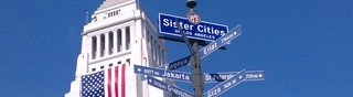 A photo of the top of LA City Hall with a portion of the "Sister Cities" mast next to it. Arrows pointing in the direction of several Los Angeles international partner cities can be seen.