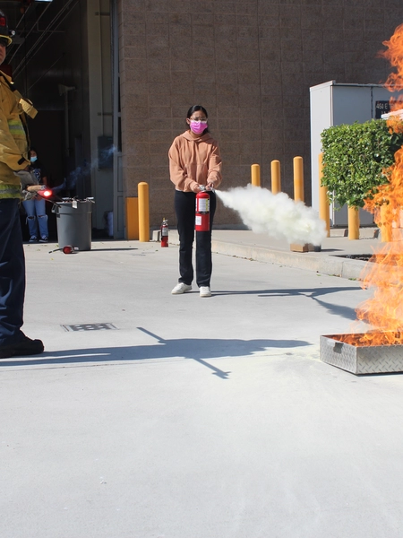 A firefighter assists a student in putting out a fire with a fire extinguisher 